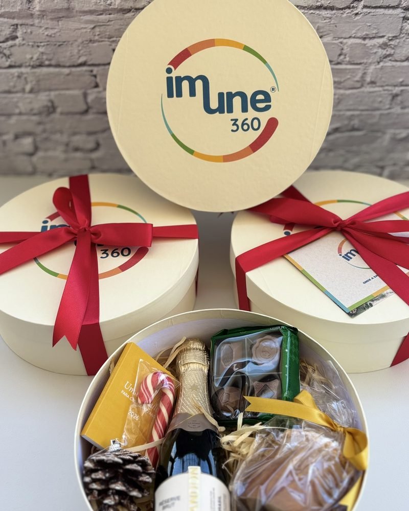 Caixas redondas com a marca Imune 360 e laço vermelho, com espumante e chocolates